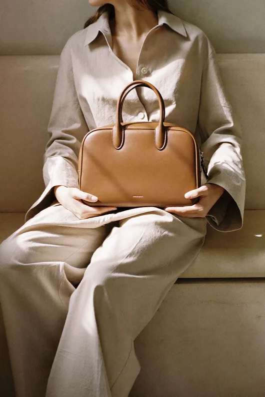 Modelo sentada segurando uma bolsa caramelo
